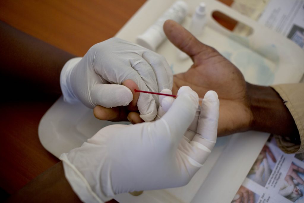 A health worker's gloved hands using a finger prick HIV test on a client.